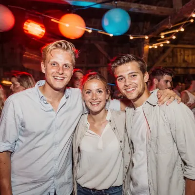 Drie vrienden arm in arm in een schuur met gekleurde lampionnen